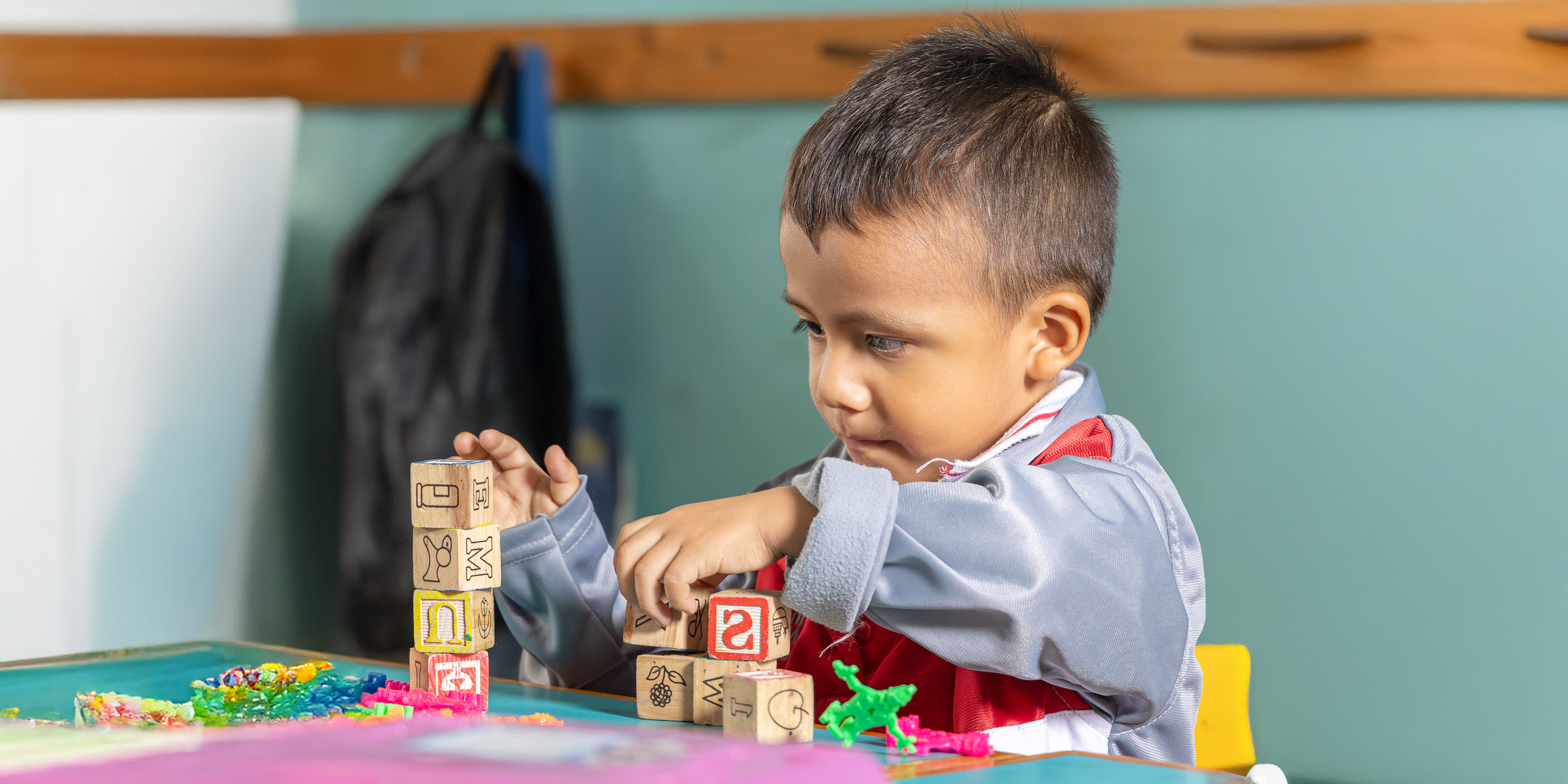 Un niño concentra su atención mientras construye torres con bloques de madera en una mesa.