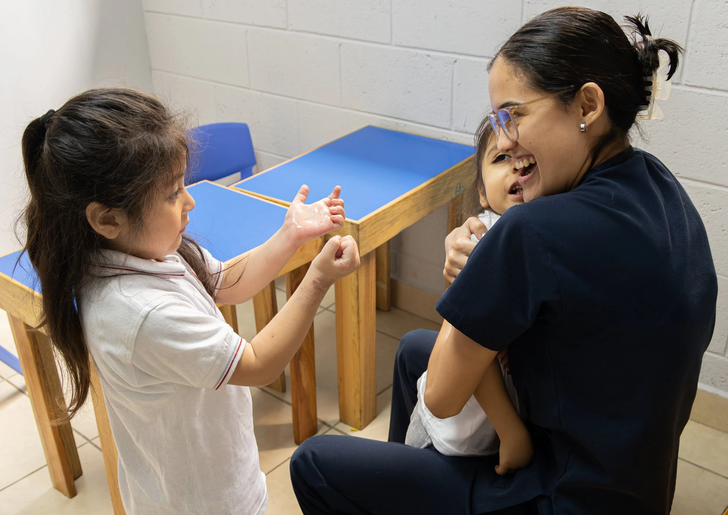 Una niña juega con una adulta que sostiene a otro niño en el aula.