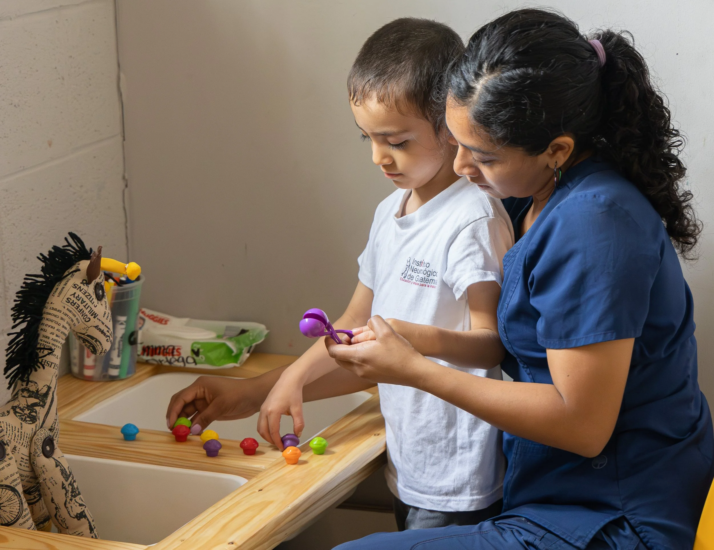 Una niña y una adulta exploran piezas de colores y maracas sobre una mesa.