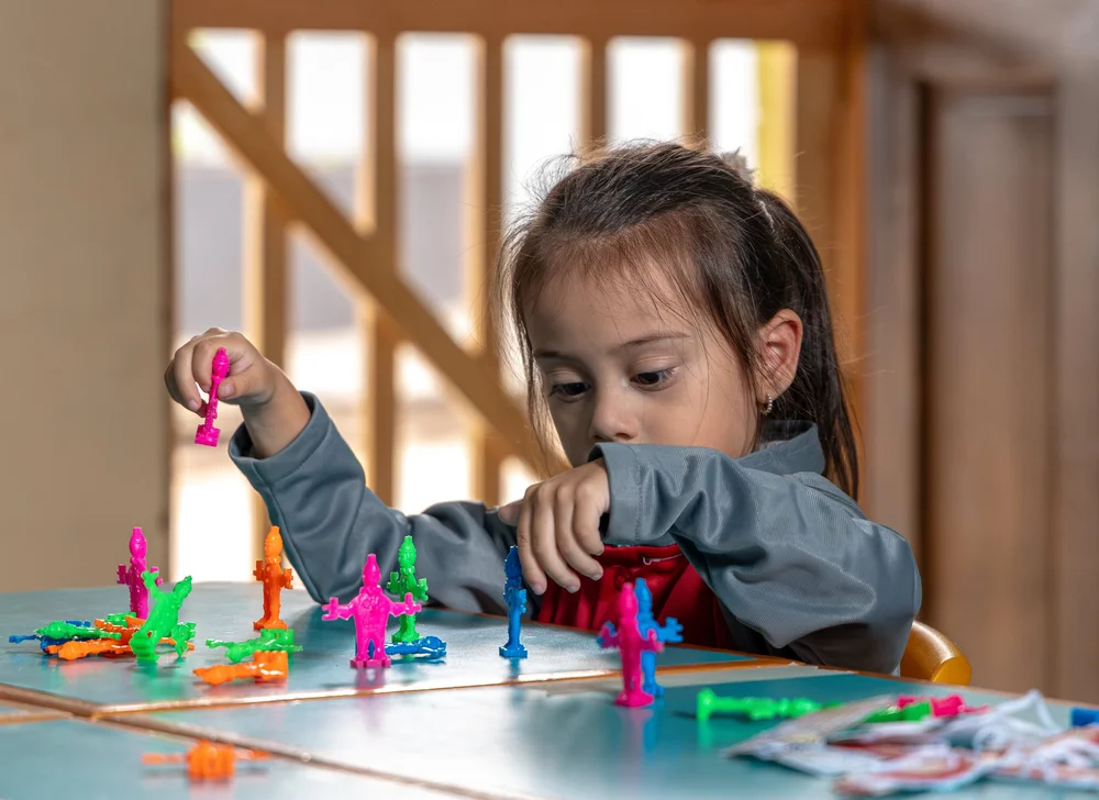 Una niña juega con figuras de colores sobre una mesa.